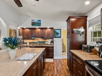 Modern kitchen on Rainbow Avenue with dark wood cabinets, a knife rack on the wall, light countertops, wood flooring, and decorative elements including flowers and artwork. - Beise Real Estate