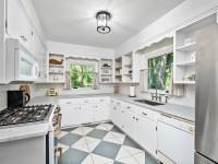 Bright Orono kitchen on Old Crystal Bay Road with white cabinets, stainless steel appliances, gray countertops, open shelving, and large windows overlooking greenery. Features a diamond-patterned tile floor. - Beise Real Estate